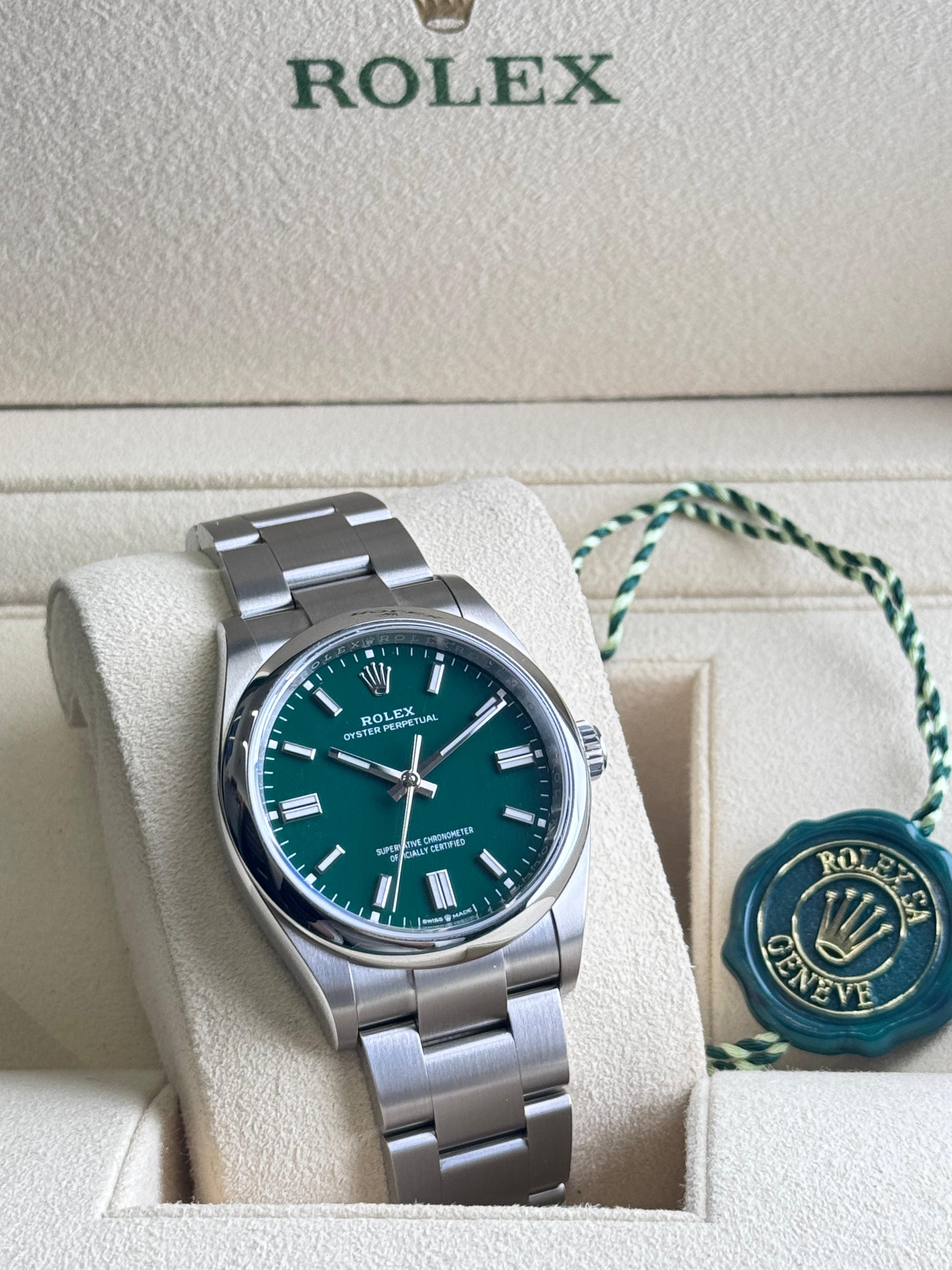Rolex watch with green face and silver bracelet on a white cushion, with 'Rolex' branding visible.